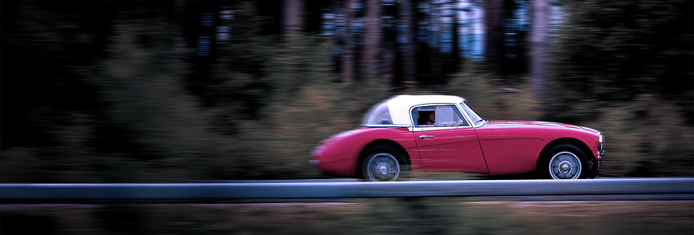 Red Austin Healey travelling on a country road at dusk